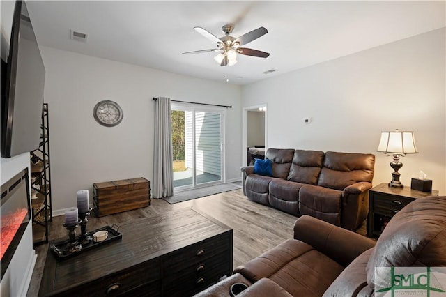 living room featuring wood finished floors, visible vents, baseboards, a ceiling fan, and a glass covered fireplace