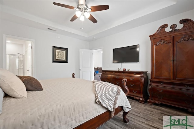 bedroom featuring visible vents, dark wood finished floors, a ceiling fan, ensuite bathroom, and a tray ceiling