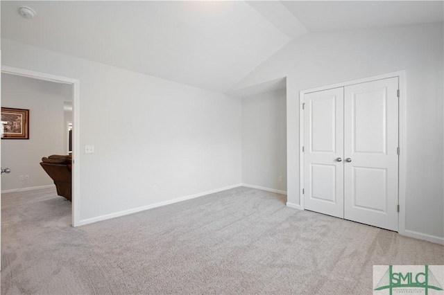 unfurnished bedroom featuring carpet, a closet, lofted ceiling, and baseboards