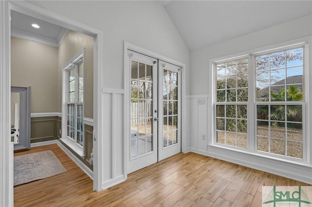 doorway to outside with lofted ceiling, wainscoting, and wood finished floors