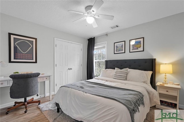 bedroom with a textured ceiling, visible vents, baseboards, a closet, and light wood finished floors