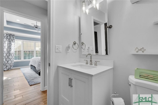 bathroom featuring toilet, wood finished floors, vanity, baseboards, and a ceiling fan