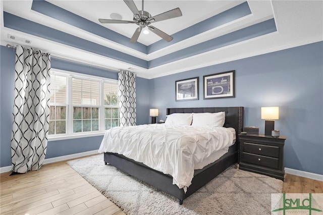 bedroom with ceiling fan, wood finished floors, a raised ceiling, and baseboards