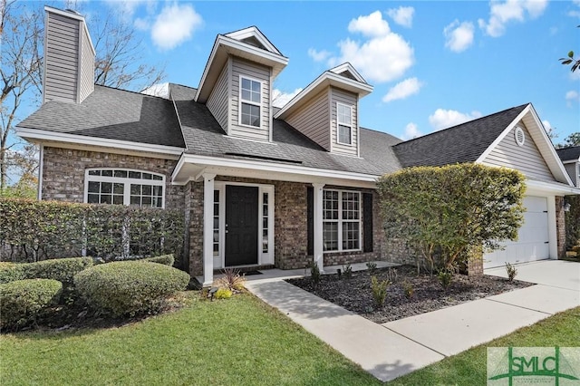 view of front of house featuring a garage, a shingled roof, concrete driveway, a front lawn, and brick siding