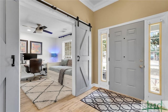 foyer featuring a barn door, a ceiling fan, light wood-style flooring, and crown molding