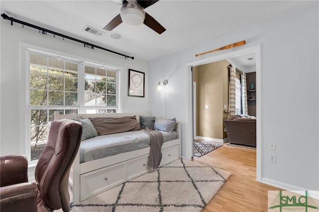 living room with a textured ceiling, visible vents, baseboards, a ceiling fan, and light wood-type flooring