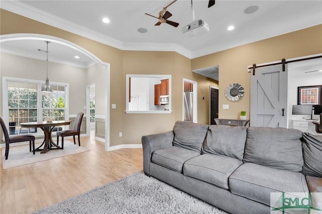 living room with light wood finished floors, a barn door, baseboards, a ceiling fan, and crown molding