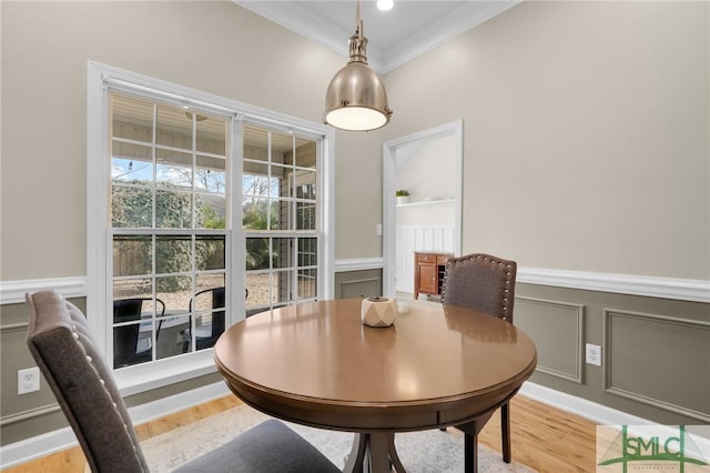 dining room featuring light wood-style flooring, ornamental molding, a decorative wall, and wainscoting