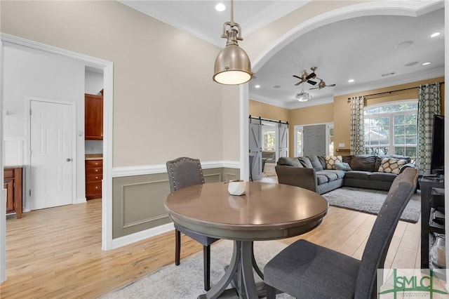 dining area with light wood-style floors, a barn door, crown molding, and wainscoting