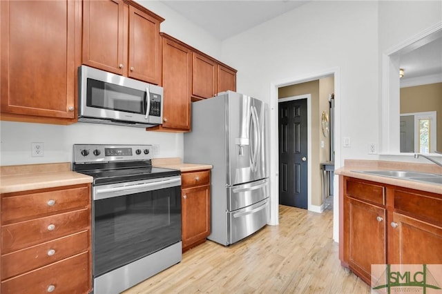 kitchen featuring stainless steel appliances, light wood finished floors, brown cabinetry, and light countertops