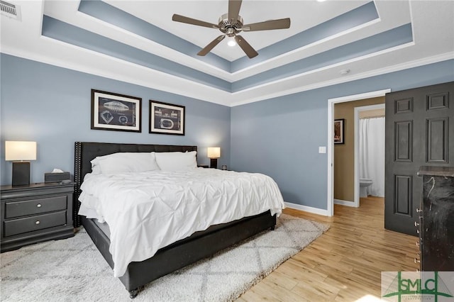 bedroom with a tray ceiling, visible vents, a ceiling fan, wood finished floors, and baseboards