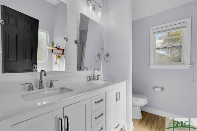 full bath featuring double vanity, wood finished floors, a sink, and toilet