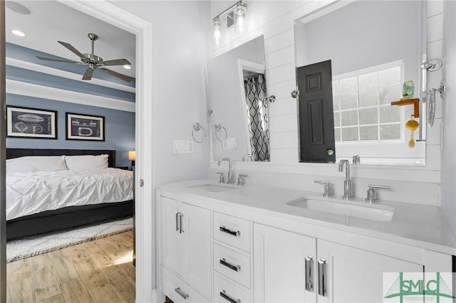 ensuite bathroom featuring double vanity, wood finished floors, a sink, and a ceiling fan