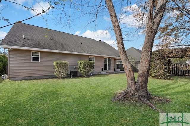 back of house with roof with shingles, a lawn, and fence