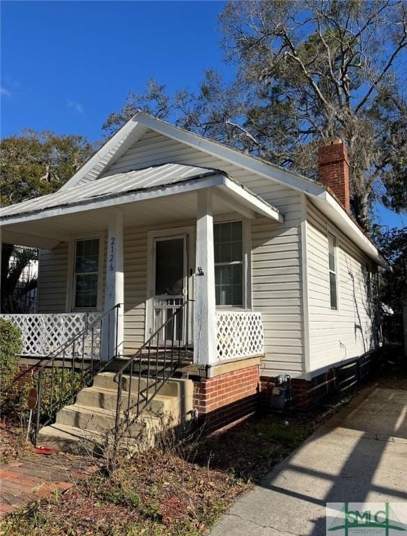 view of front of property featuring metal roof, a chimney, and a porch