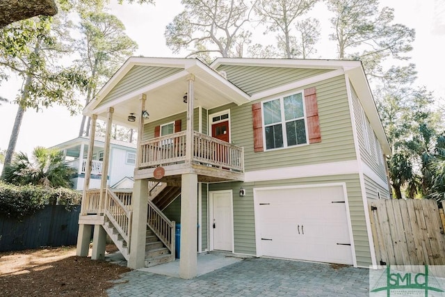 coastal inspired home with an attached garage, stairs, fence, and decorative driveway