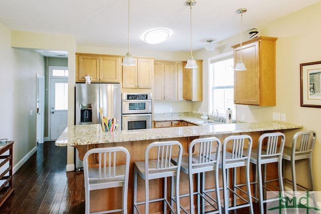 kitchen featuring stainless steel appliances, a peninsula, dark wood-style flooring, a sink, and light stone countertops