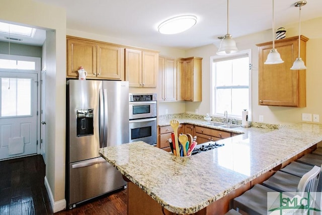 kitchen with dark wood-type flooring, a peninsula, stainless steel appliances, a kitchen bar, and a sink