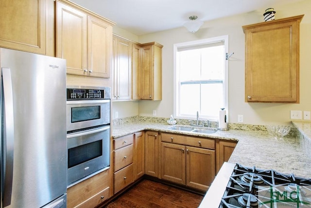 kitchen featuring stainless steel appliances, dark wood-type flooring, a sink, and light stone countertops