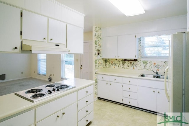 kitchen with white appliances, white cabinets, light countertops, under cabinet range hood, and a sink