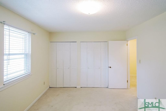 unfurnished bedroom featuring a textured ceiling, baseboards, two closets, and light colored carpet