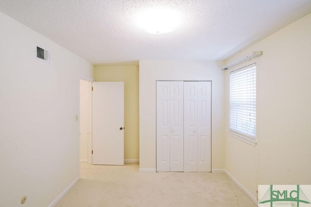 unfurnished bedroom with a textured ceiling, a closet, visible vents, and light colored carpet