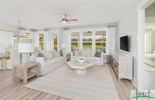 living area featuring light wood-type flooring and ceiling fan with notable chandelier