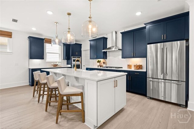 323 Birch Dr, Richmond Hill, GA 31324 - kitchen featuring stainless steel appliances, wall chimney exhaust hood, backsplash, light countertops, and blue cabinetry