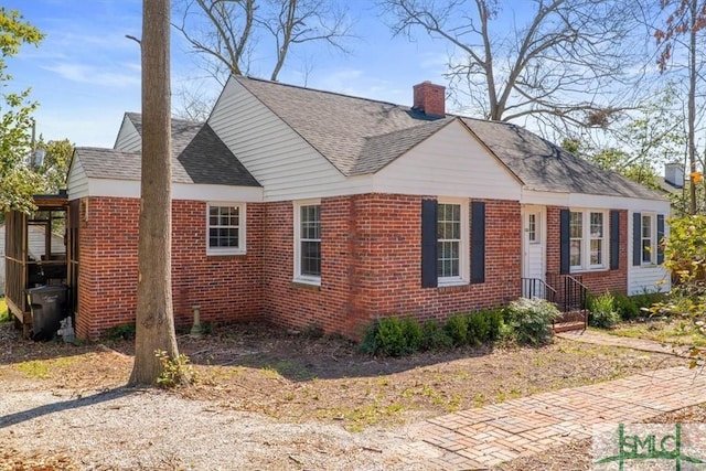 view of front facade featuring brick siding, a chimney, and roof with shingles