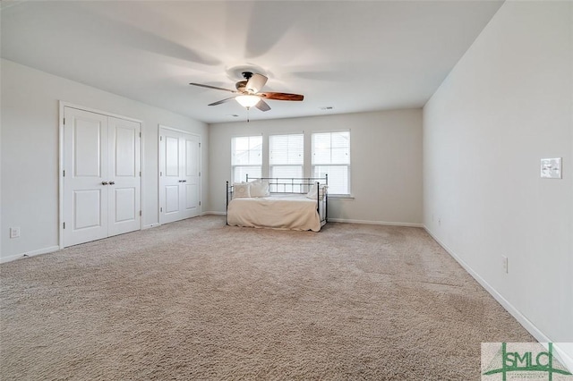 unfurnished bedroom with multiple closets, light carpet, ceiling fan, and baseboards