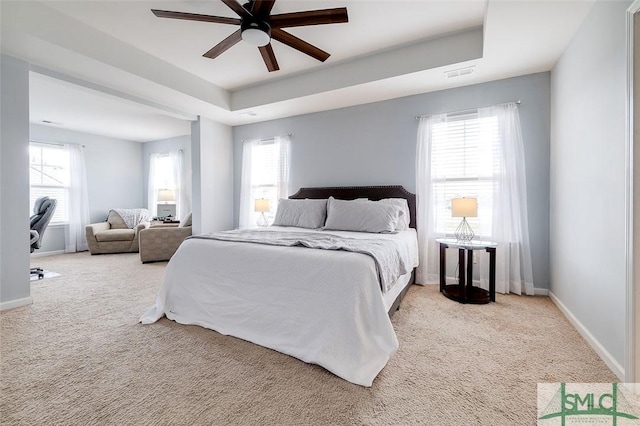 carpeted bedroom with a ceiling fan, a raised ceiling, visible vents, and baseboards