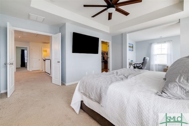 bedroom with visible vents, baseboards, light colored carpet, a spacious closet, and a tray ceiling