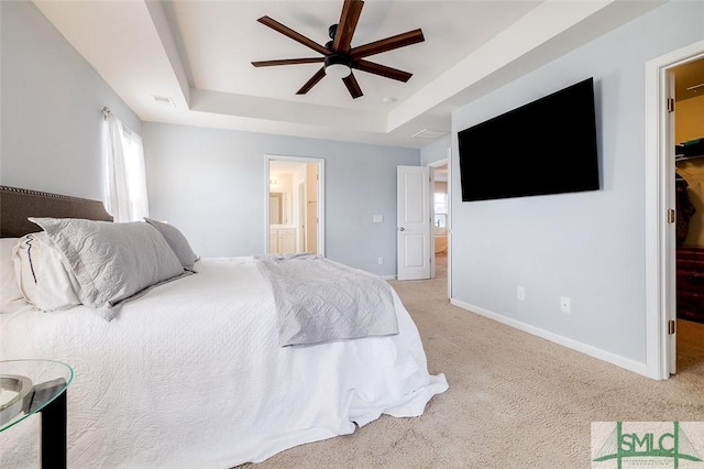 carpeted bedroom with ensuite bathroom, a ceiling fan, baseboards, a spacious closet, and a raised ceiling