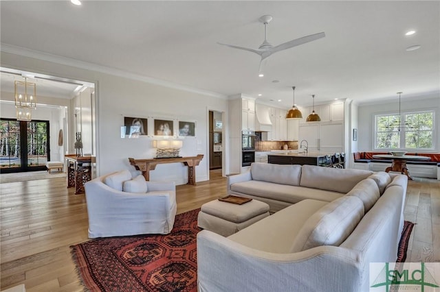 living area with recessed lighting, crown molding, light wood-style flooring, and ceiling fan with notable chandelier