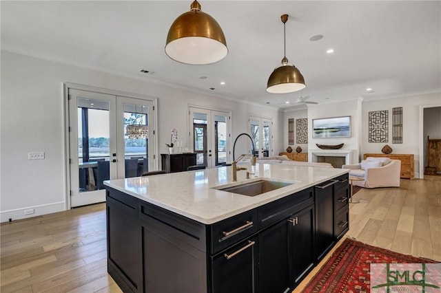 kitchen with light wood-style flooring, dark cabinets, a fireplace, a sink, and french doors