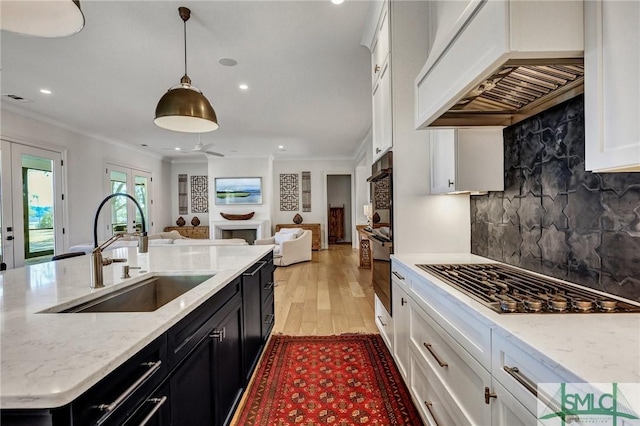 kitchen featuring french doors, dark cabinetry, stainless steel gas stovetop, a sink, and premium range hood