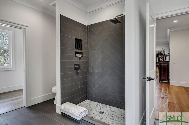 bathroom featuring toilet, wood finished floors, baseboards, ornamental molding, and a tile shower