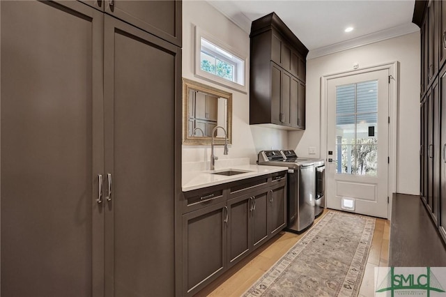 laundry room with cabinet space, light wood-style flooring, ornamental molding, washing machine and dryer, and a sink