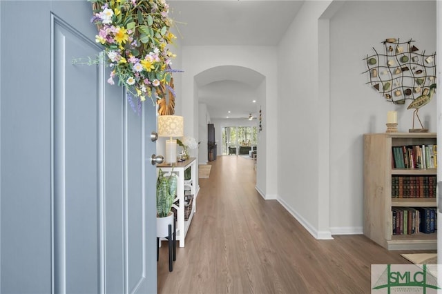 corridor with arched walkways, baseboards, and wood finished floors