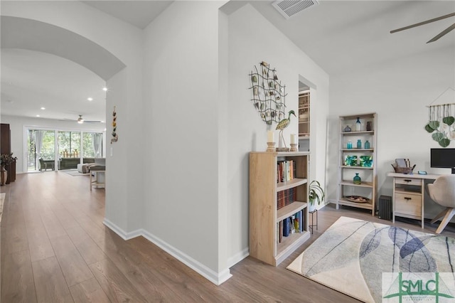 corridor with baseboards, visible vents, arched walkways, and wood finished floors