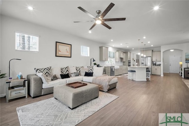 living area with light wood-type flooring, arched walkways, a ceiling fan, and recessed lighting