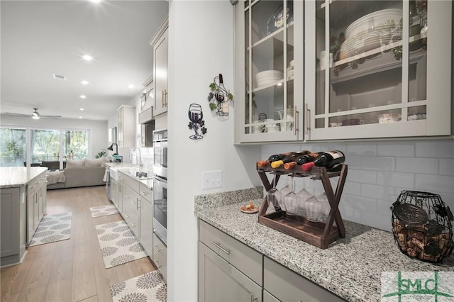 kitchen with decorative backsplash, light wood-style flooring, light stone counters, glass insert cabinets, and open floor plan