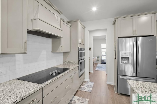 kitchen with light stone counters, light wood finished floors, custom exhaust hood, decorative backsplash, and appliances with stainless steel finishes