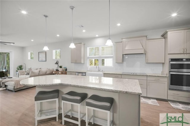 kitchen featuring a breakfast bar, custom exhaust hood, double oven, open floor plan, and a sink