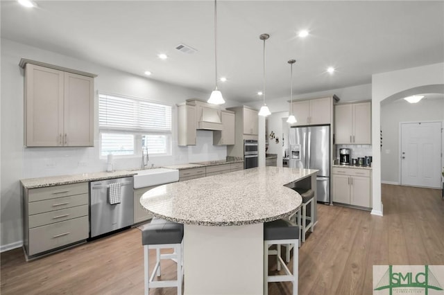 kitchen featuring arched walkways, stainless steel appliances, a sink, and gray cabinetry