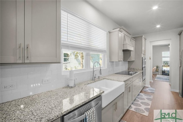 kitchen with tasteful backsplash, light stone counters, stainless steel appliances, light wood-style floors, and a sink