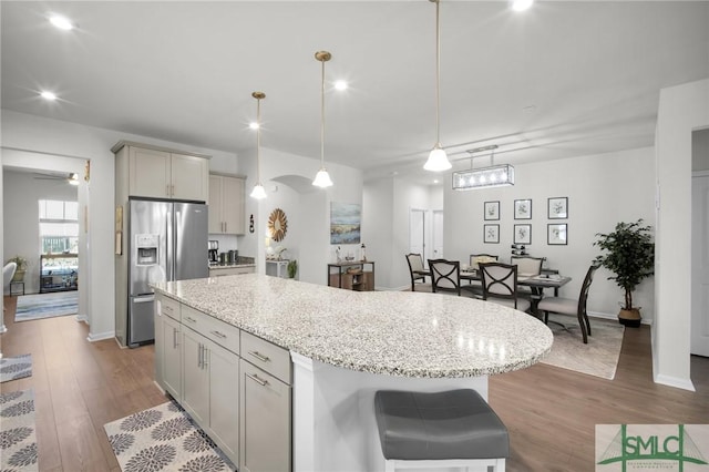 kitchen with arched walkways, dark wood finished floors, stainless steel fridge with ice dispenser, a kitchen island, and pendant lighting