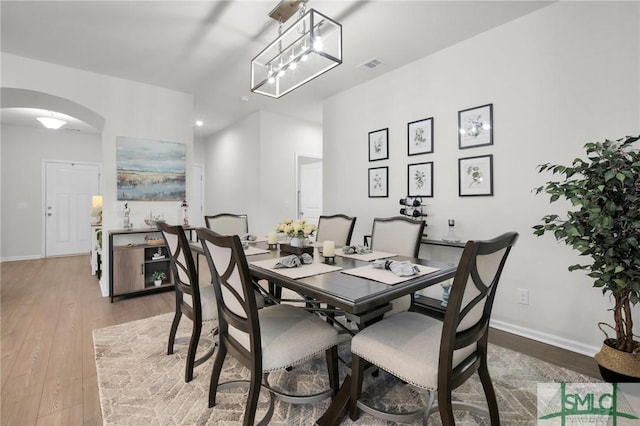 dining space with light wood finished floors, baseboards, visible vents, and arched walkways