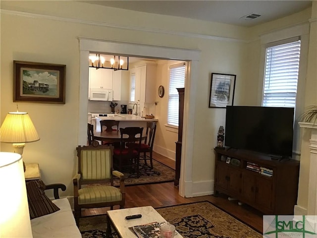 living area with baseboards, wood finished floors, visible vents, and an inviting chandelier