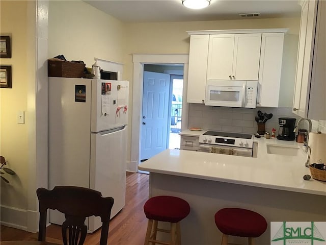 kitchen featuring tasteful backsplash, light countertops, a sink, white appliances, and a peninsula